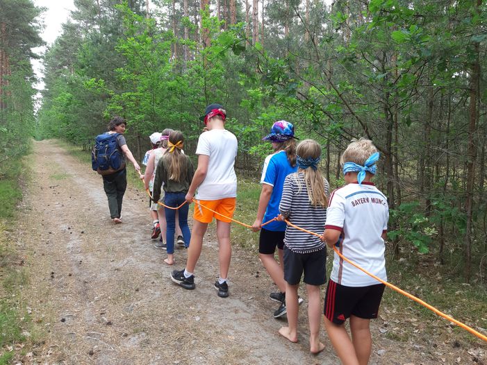 Eine Pädagogin führt eine Kindergruppe durch den Wald